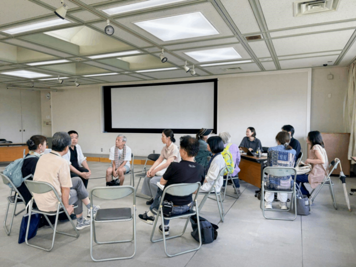 会議室で椅子を円形に並べ、10人ほどの男女が座って話し合っている様子。